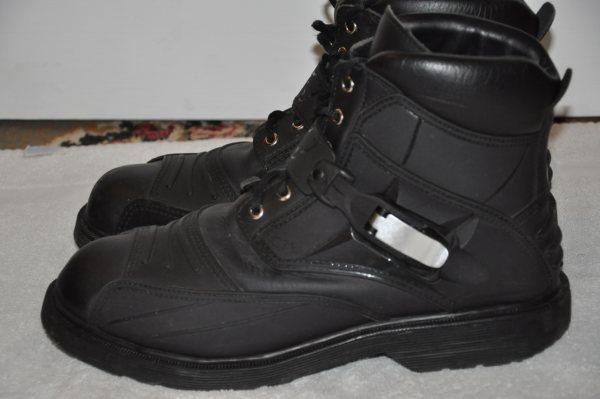 Pair of black leather motorcycle boots with laces and side buckle, side view indoors