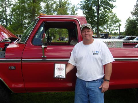 2007 Ford Mustang - Man with award poses by a red 1973 Ford F-250 truck at an outdoor event with other vehicles present.