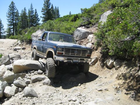 1986 Ford Bronco - A blue Ford Bronco is shown traversing a challenging, rocky off-road path.