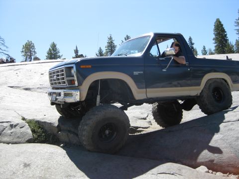 1986 Ford Bronco - This lifted Ford Bronco is navigating a rocky trail under a clear blue sky.