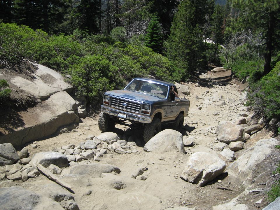 Blue Ford pickup truck with lifted suspension navigating a rocky off-road trail