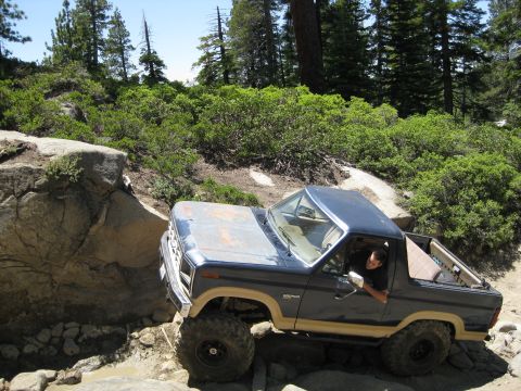 1986 Ford Bronco - This Ford Bronco is shown off-roading on a , rocky trail surrounded by trees and brush.