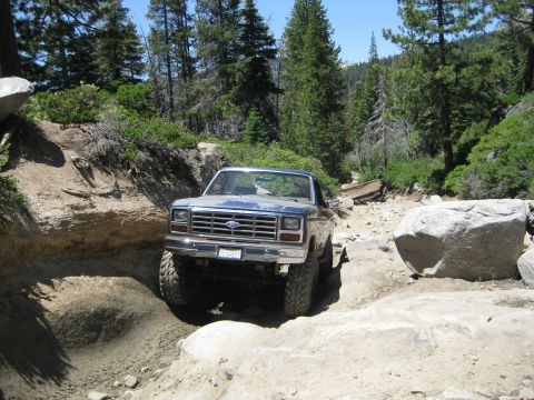 1986 Ford Bronco - This Ford Bronco is tackling a challenging off-road path with large rocks and steep inclines.