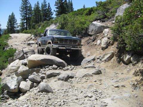 1986 Ford Bronco - A dark blue 1980 Ford Bronco navigates a challenging, rocky off-road path.