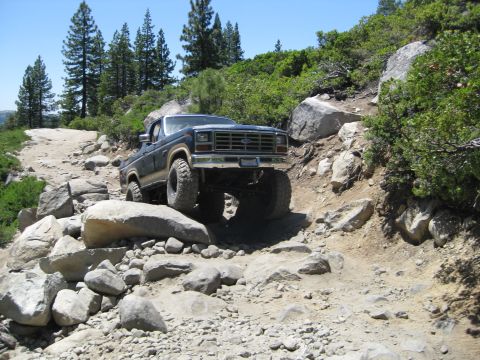 1986 Ford Bronco - This lifted 4x4 truck navigates a challenging rocky trail under a clear blue sky.