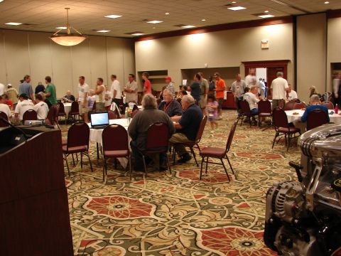 1992 Ford Taurus - A convention hall is set up with tables and chairs, hosting an event with attendees mingling and a car engine displayed.