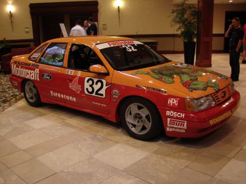 1992 Ford Taurus - A 1992 Ford Taurus race car, adorned with Teenage Mutant Ninja Turtle graphics and sponsor decals, is displayed indoors.