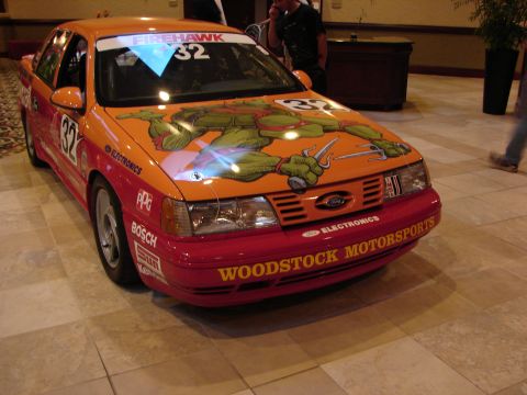 1992 Ford Taurus - This 1992 Ford Taurus sports a vibrant orange and red livery, complete with Teenage Mutant Ninja Turtle graphics and racing numbers.