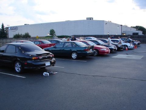 1992 Ford Taurus - Several cars are parked in a lot outside a large building, with a black Ford Taurus in the foreground.