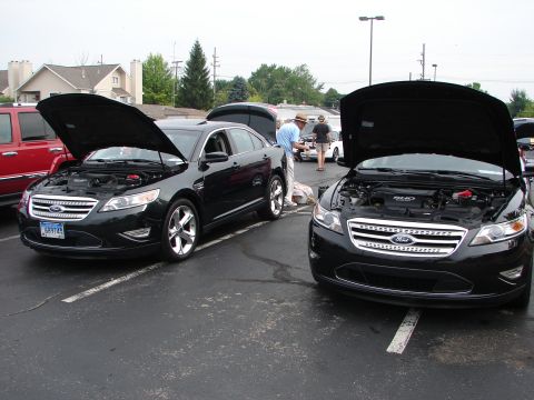 1992 Ford Taurus - Two black Ford Taurus sedans are displayed with their hoods open at a convention.