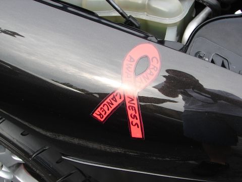 1992 Ford Taurus - A red ribbon sticker promoting cancer awareness is affixed to the glossy black hood of a vehicle.