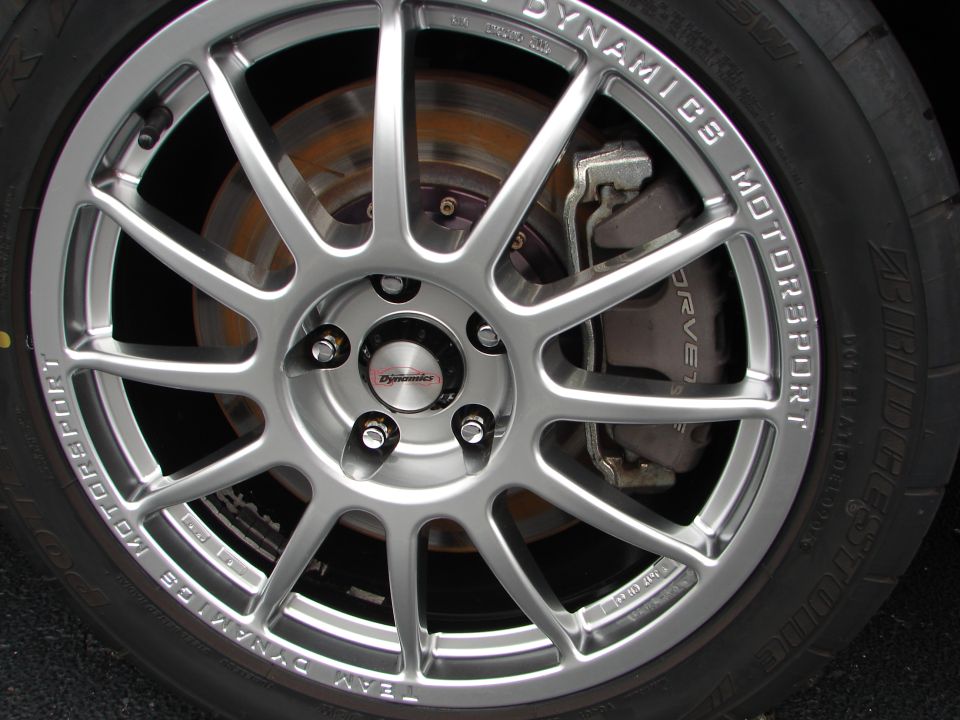 Close-up of a silver multi-spoke wheel with 'TEAM DYNAMICS MOTORSPORT' text, showing a brake caliper and rotor
