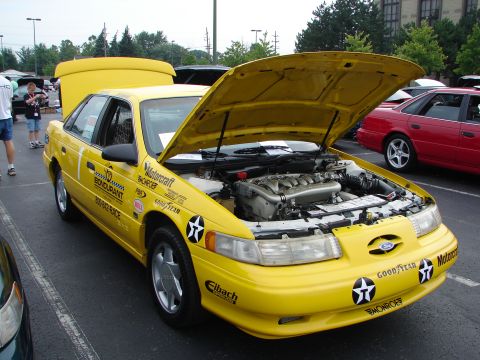 1992 Ford Taurus - A yellow 1992 Ford Taurus sedan is displayed with its hood open, revealing the engine and adorned with various decals.