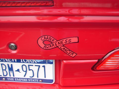 1992 Ford Taurus - A red car's rear shows a license plate and a sticker promoting cancer awareness.