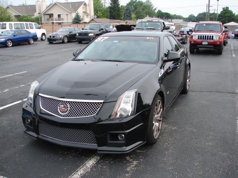1992 Ford Taurus - A black Cadillac CTS sedan is parked in a lot with other vehicles, displaying race numbers on its windshield.