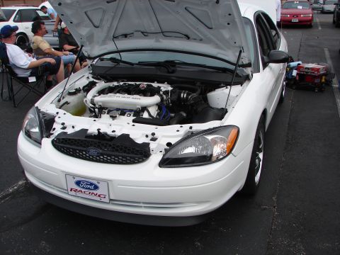 1992 Ford Taurus - A white Ford Taurus is displayed with its hood open, revealing the engine and a Ford Racing license plate.