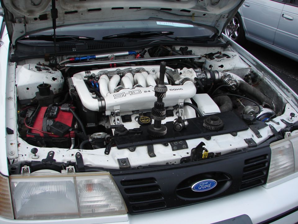 White 1992 Ford Taurus engine bay with SHO 24V DOHC engine, red battery, and Ford grille