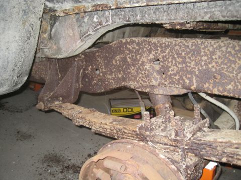 1979 Ford Bronco - Close-up view of heavily rusted suspension components, including a leaf spring and frame section, with a brake drum visible.