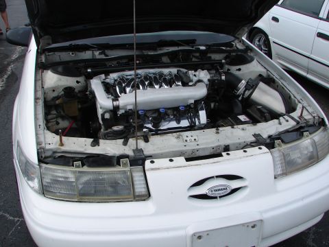 1992 Ford Taurus - The engine bay of a 1992 Ford Taurus, a custom intake and a Yamaha badge on the grille, with another white car visible in the background.