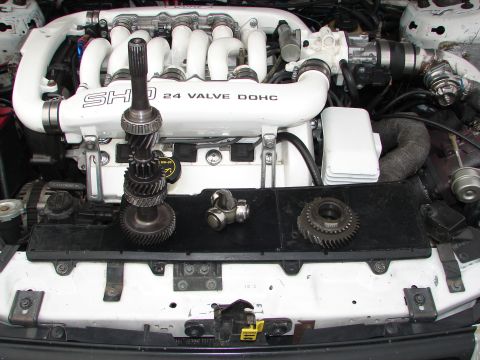 1992 Ford Taurus - Engine components, including gears and a driveshaft, are laid out in front of an engine block labeled "SHO 24 VALVE DOHC".