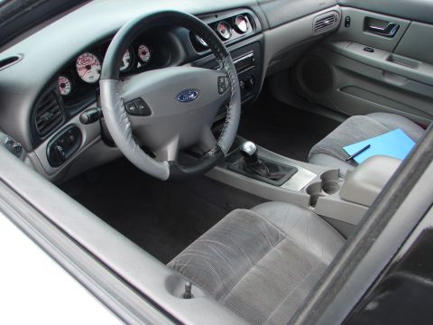 1992 Ford Taurus - The interior of a car features aftermarket gauges and a manual transmission shifter, with a notepad resting on the passenger seat.