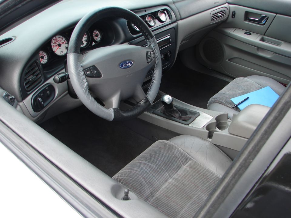 car interior with aftermarket gauges, manual shifter, and a blue notepad on the passenger seat