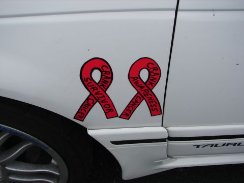 1992 Ford Taurus - Red cancer awareness ribbons are affixed to the side of a white vehicle.