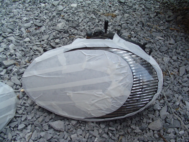 Car headlight covered in masking tape, resting on gravel