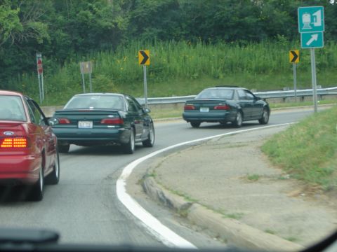 1992 Ford Taurus - Two dark green sedans drive on a highway, one in front of the other.