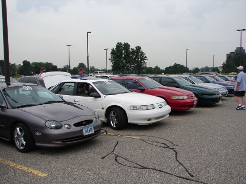 1992 Ford Taurus - Multiple Ford Taurus models from 1992 are lined up at an event, with one car's hood open.
