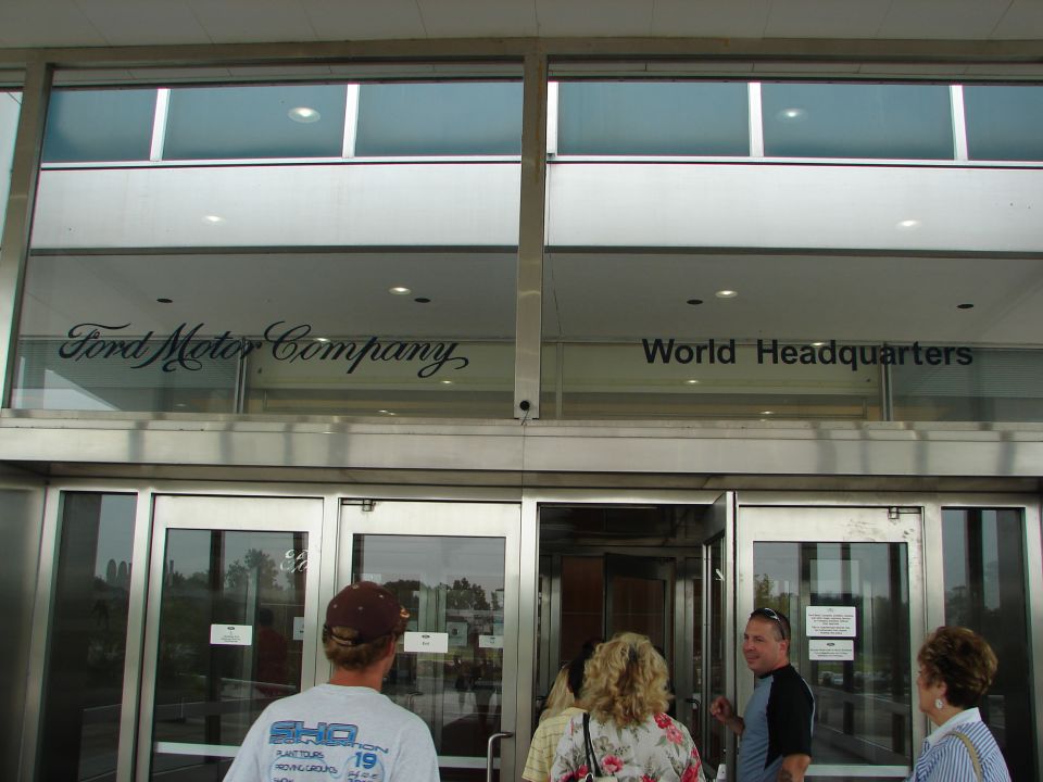 People entering Ford Motor Company World Headquarters. Text on building says 'Ford Motor Company' and 'World Headquarters'