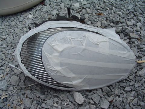 1999 Ford Taurus - A car headlight assembly, partially covered with tape, lies on a bed of grey gravel.