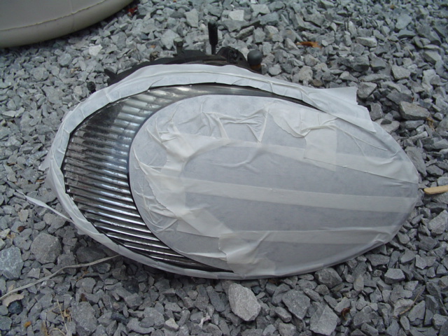 Headlight assembly covered in masking tape, resting on gravel