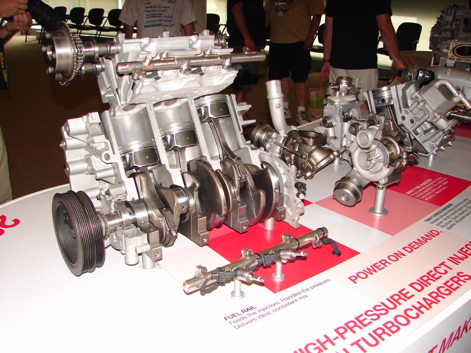 Cutaway engine with visible pistons, crankshaft, and twin turbochargers. Fuel rail in foreground