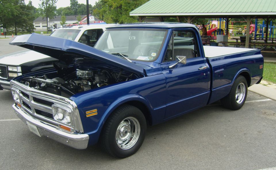 Blue pickup truck with hood open, showing engine. Another white truck is partially visible behind it