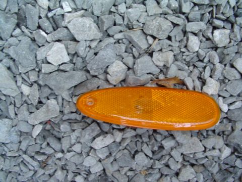 1999 Ford Taurus - An orange side marker light is shown lying on a bed of gray gravel.