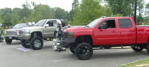 2007 Ford Mustang - Two lifted pickup trucks are parked side-by-side at an outdoor event, displaying custom wheels and modifications.