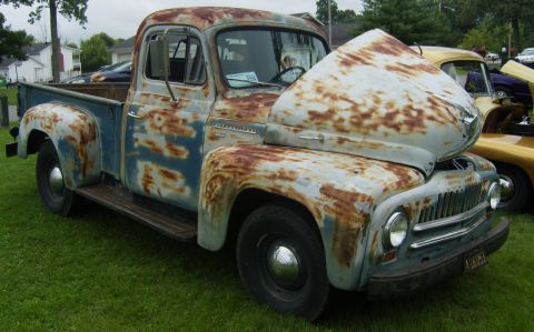 2007 Ford Mustang - A heavily rusted blue and white pickup truck is displayed with its hood open at an outdoor event.