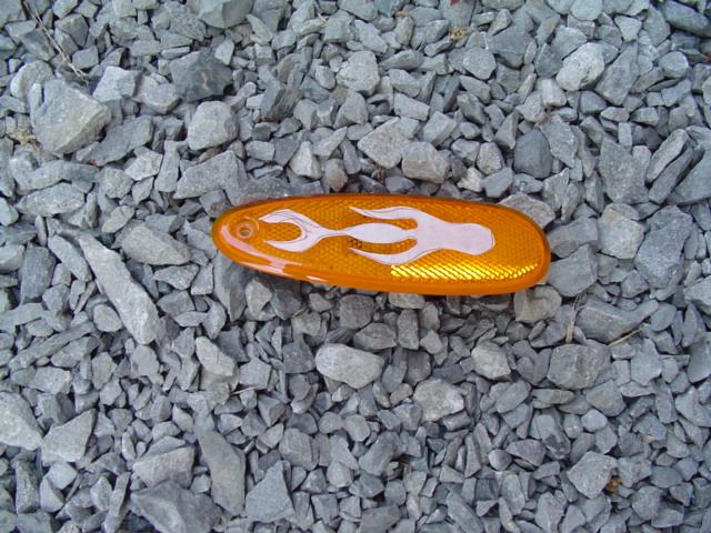 Orange oval side marker with white flame decal on gravel