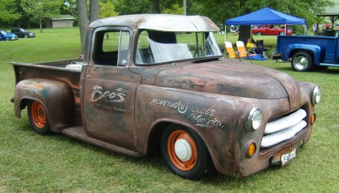 2007 Ford Mustang - A heavily rusted pickup truck with custom lettering on its doors sits on a grassy field at an outdoor event.