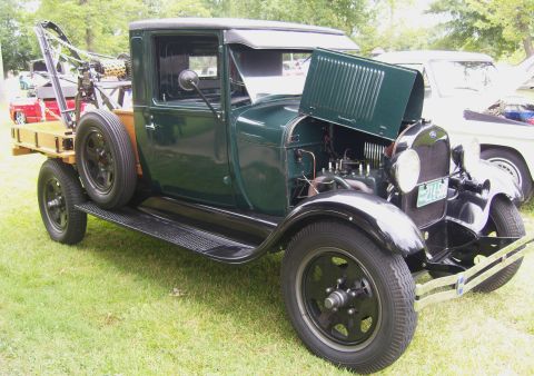 2007 Ford Mustang - Vintage green tow truck with a wooden bed and spare tire, hood open, parked on grass.