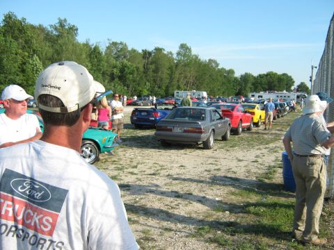 1985 Ford Mustang - A line of cars, including a gray 1985 Ford Mustang, are parked at an outdoor event.