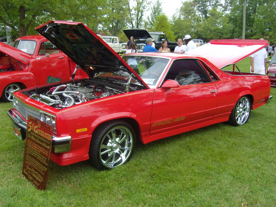 red El Camino with hood and trunk open, custom wheels, and a display sign in front