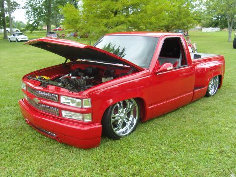 2007 Ford Mustang - A red pickup truck with its hood open and chrome wheels sits on a grassy field.