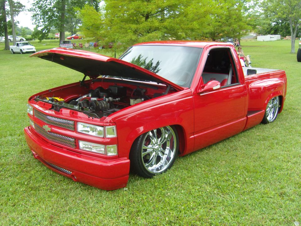 Red pickup truck with hood open, chrome wheels, and lowered suspension