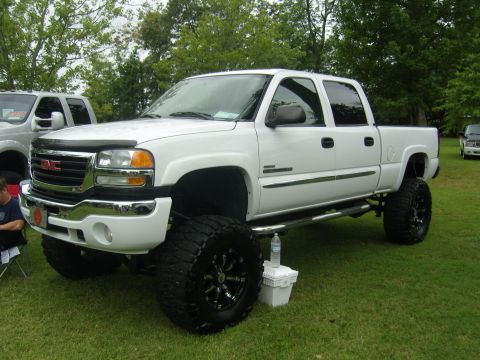 2007 Ford Mustang - White GMC Sierra pickup truck with lifted suspension and large off-road tires parked on grass.