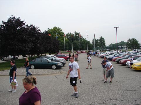 1992 Ford Taurus - A gathering of people and vehicles in an outdoor parking lot under an overcast sky.