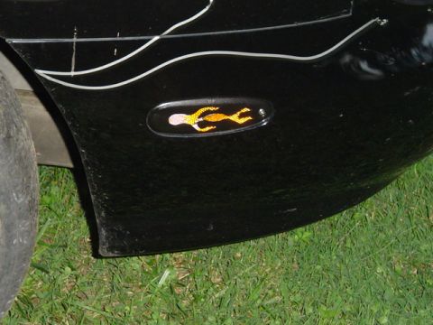 1999 Ford Taurus - A black car fender displays a flame decal on its side marker light, with white pinstriping and a portion of a tire visible.
