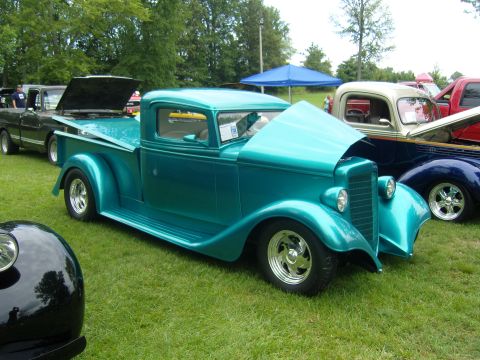 2007 Ford Mustang - A teal-colored vintage pickup truck is displayed at an outdoor car show, with its hood open.
