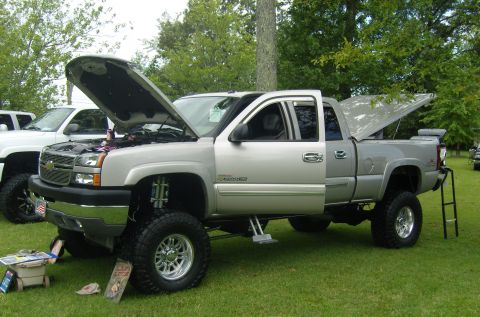2007 Ford Mustang - Silver Chevrolet Silverado pickup truck with aftermarket modifications, hood and bed cover open, parked on grass.